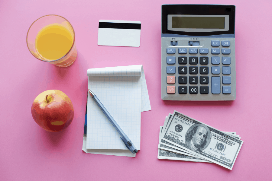 calculator, money and fruit on a pink tabletop