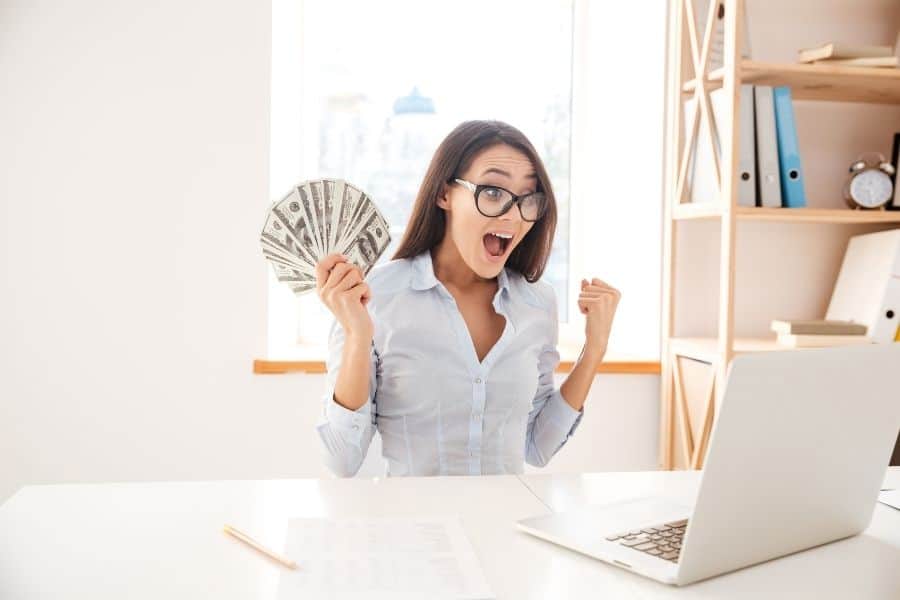 woman holding cash and looking at a laptop