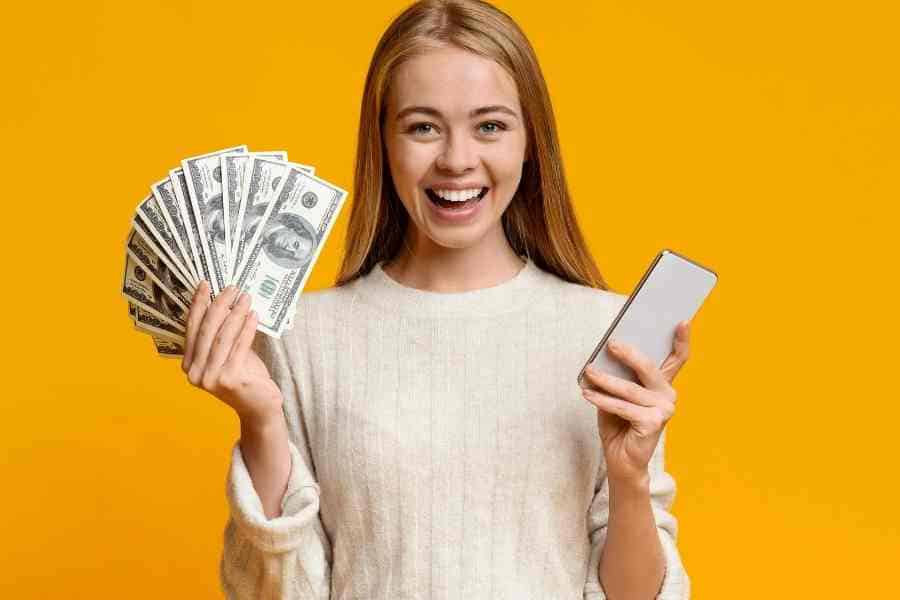 teen girl holding cash in one hand and a phone in the other