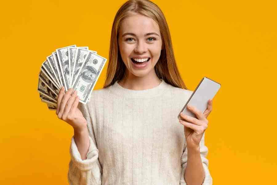 teen girl holding cash in one hand and a phone in the other